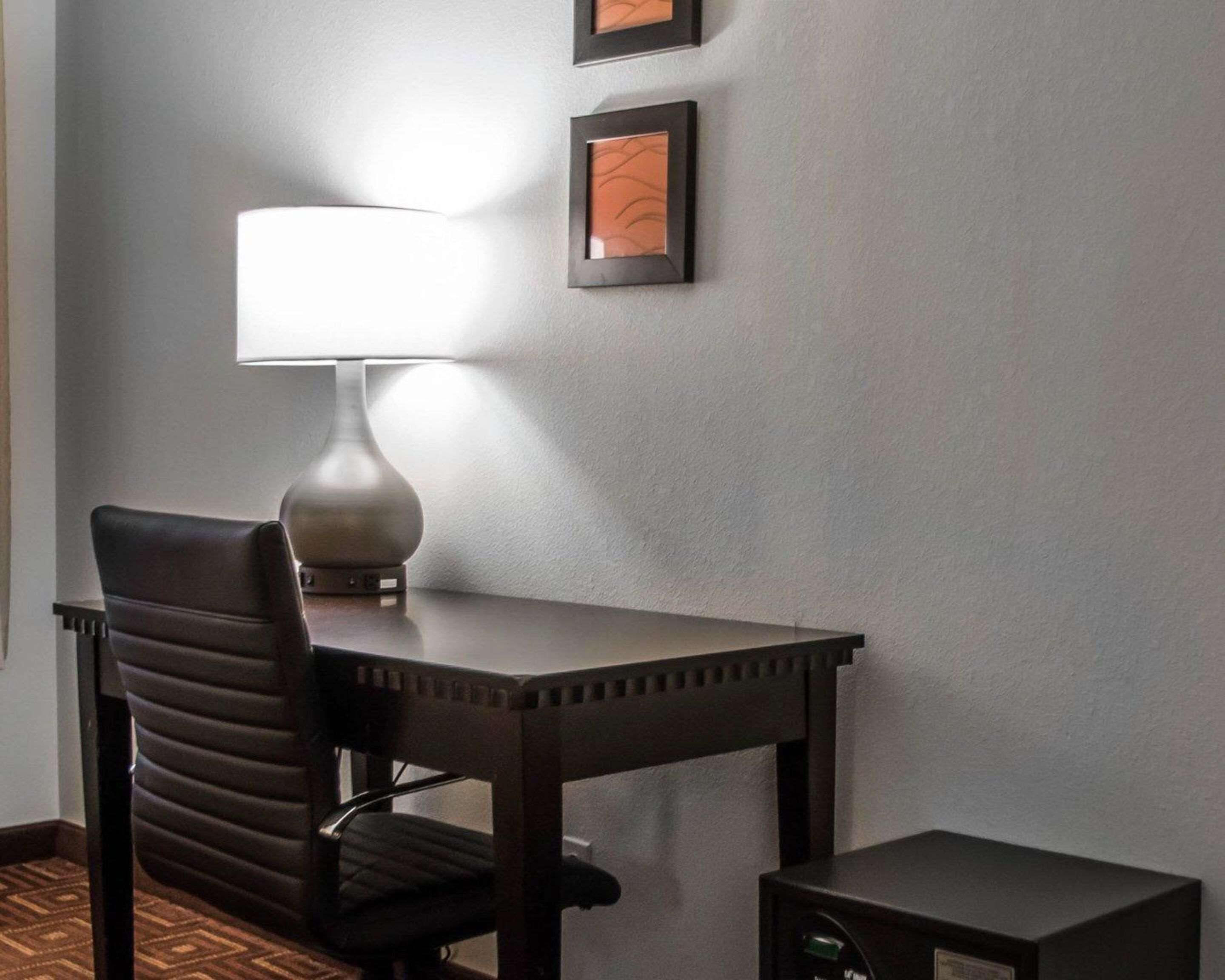 A hotel room with a desk, chair, lamp, and a small table.