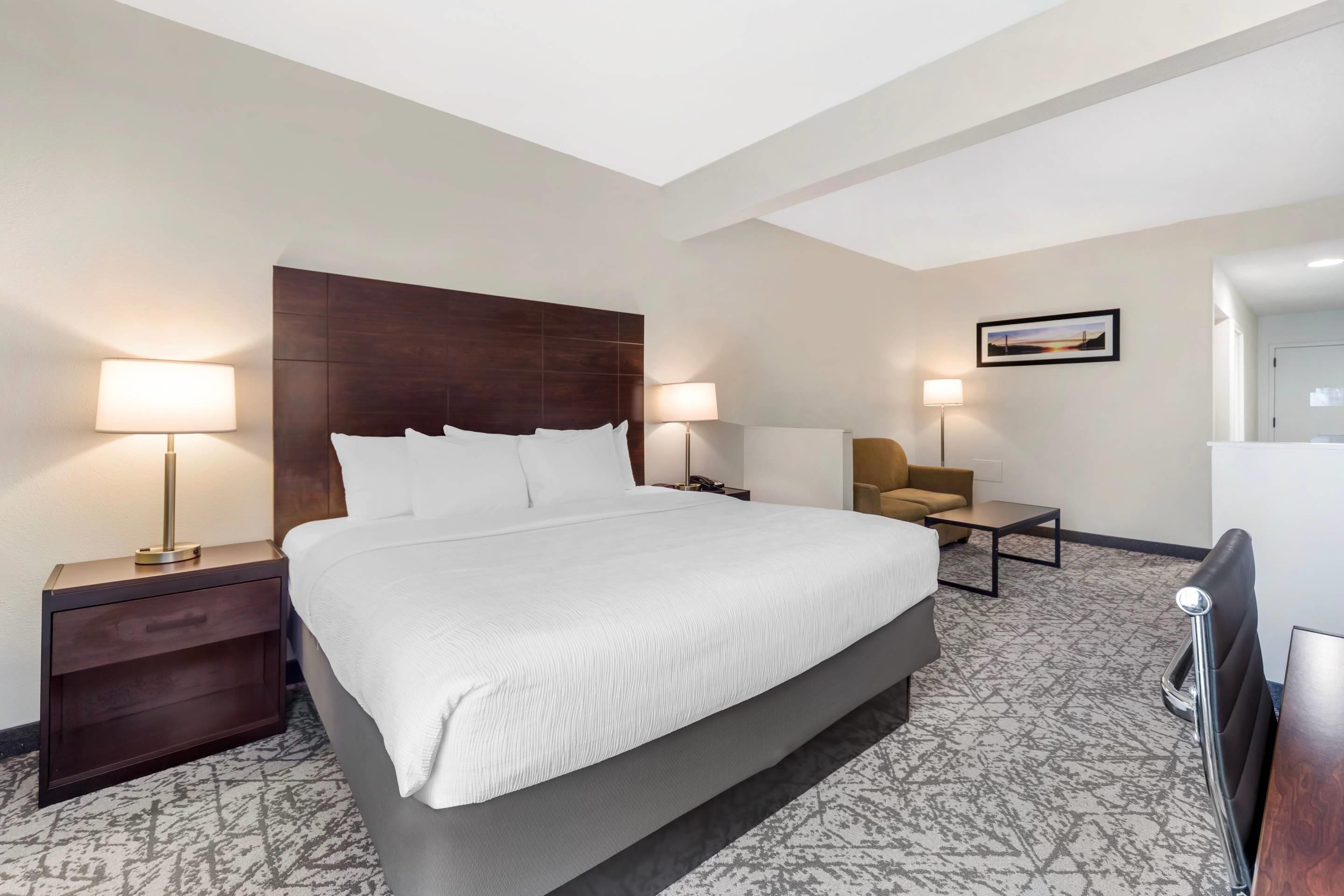 Una habitación de hotel con una cama grande, dos mesitas de noche con lámparas, un pequeño sofá y un escritorio.
