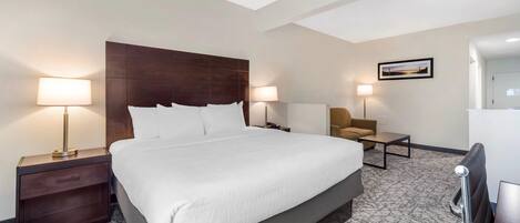 Una habitación de hotel con una cama grande, dos mesitas de noche con lámparas, un pequeño sofá y un escritorio.
