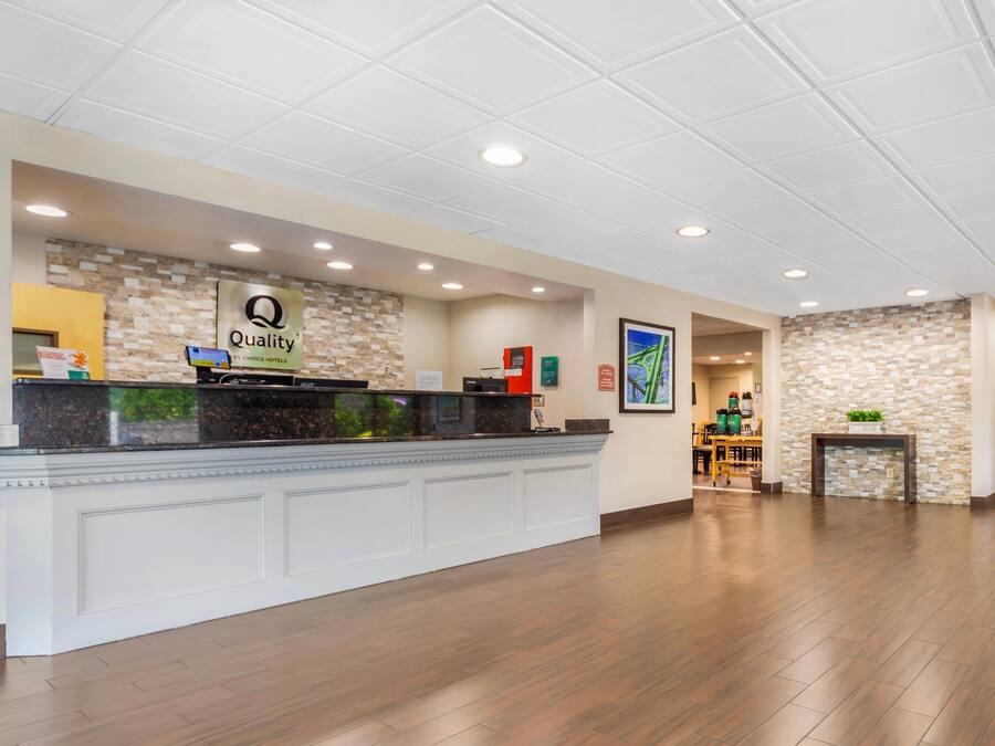 A hotel reception area with a reception desk, a sign reading "Quality by Choice Hotels," and a stone wall.