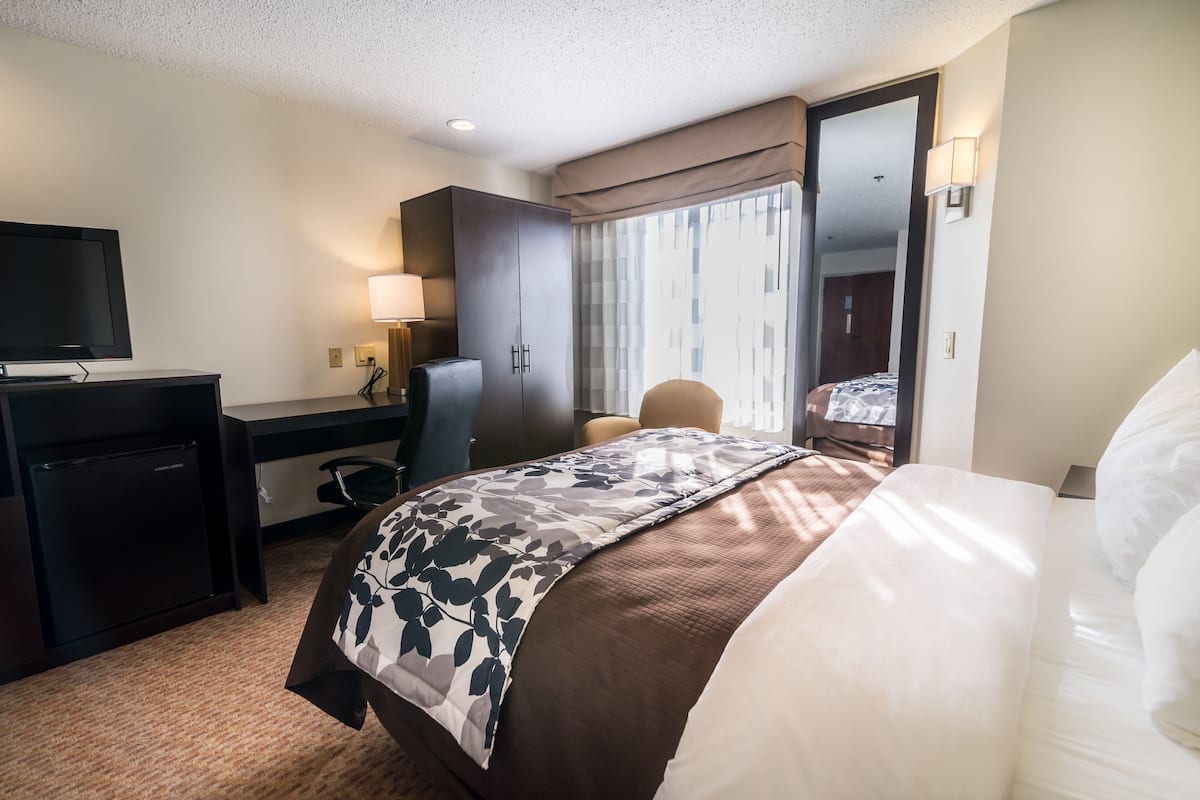 Une chambre d’hôtel comprenant un lit, un bureau avec un ordinateur, une télévision, une chaise et une armoire.