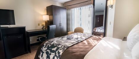A hotel room with a bed, a desk with a computer, a TV, a chair, and a wardrobe.