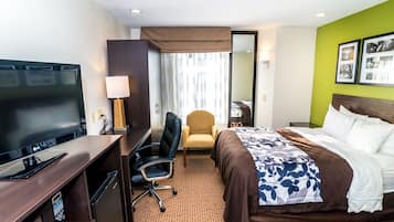 A hotel room with a bed, a desk with a TV, a chair, and a mirror.
