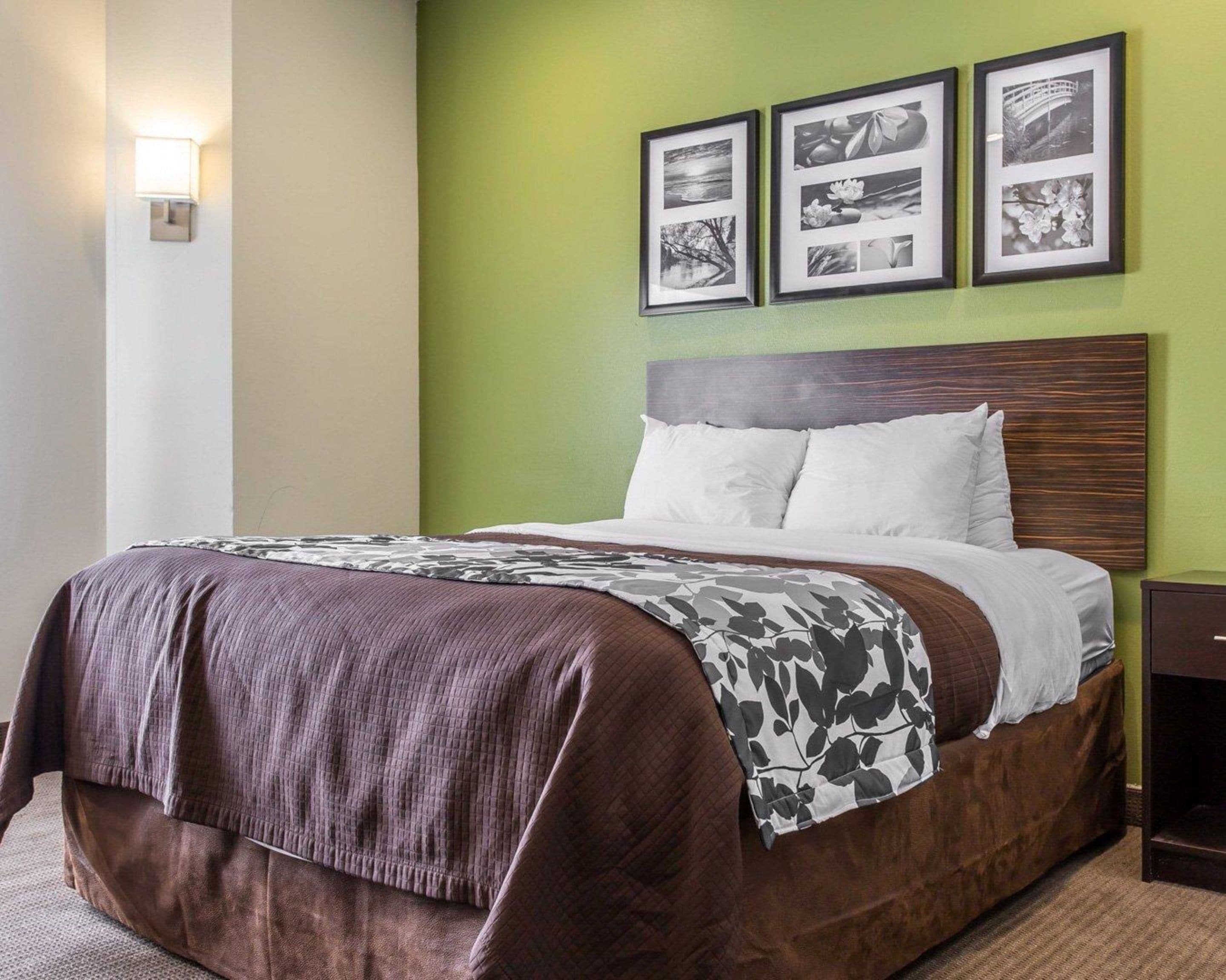 Een net opgemaakt bed met een bruin-wit geborreld beddengoed, een houten hoofdbord en drie ingelijste zwart-wit foto’s aan de muur.