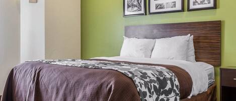Un letto rifatto con cura, con copripiumino marrone e bianco a motivi decorativi, una testiera in legno e tre fotografie in bianco e nero incorniciate appese al muro.