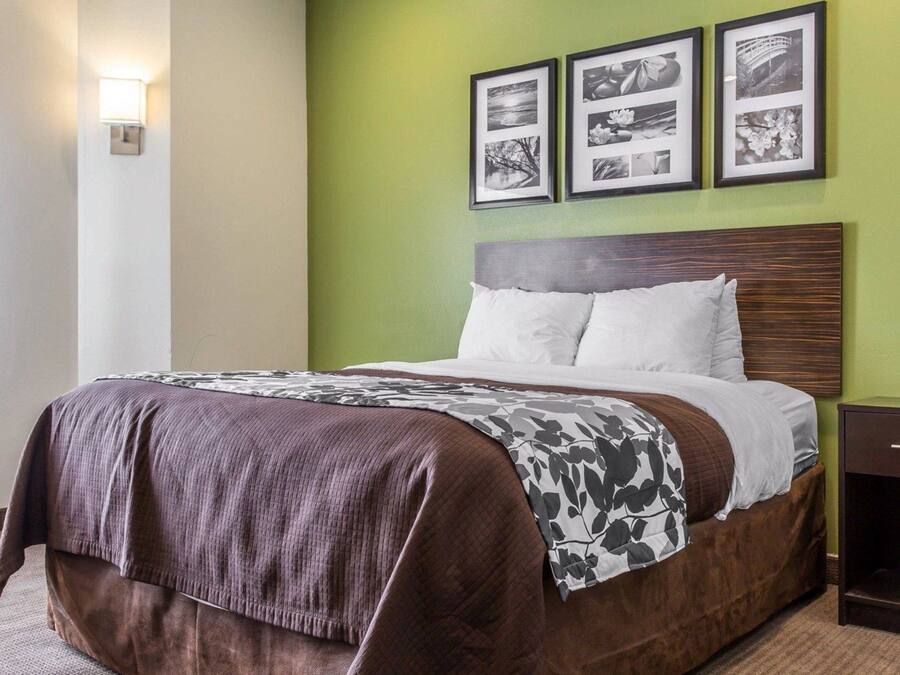 Una cama bien tendida con una colcha marrón y blanca estampada, un cabecero de madera y tres fotografías en blanco y negro enmarcadas en la pared.