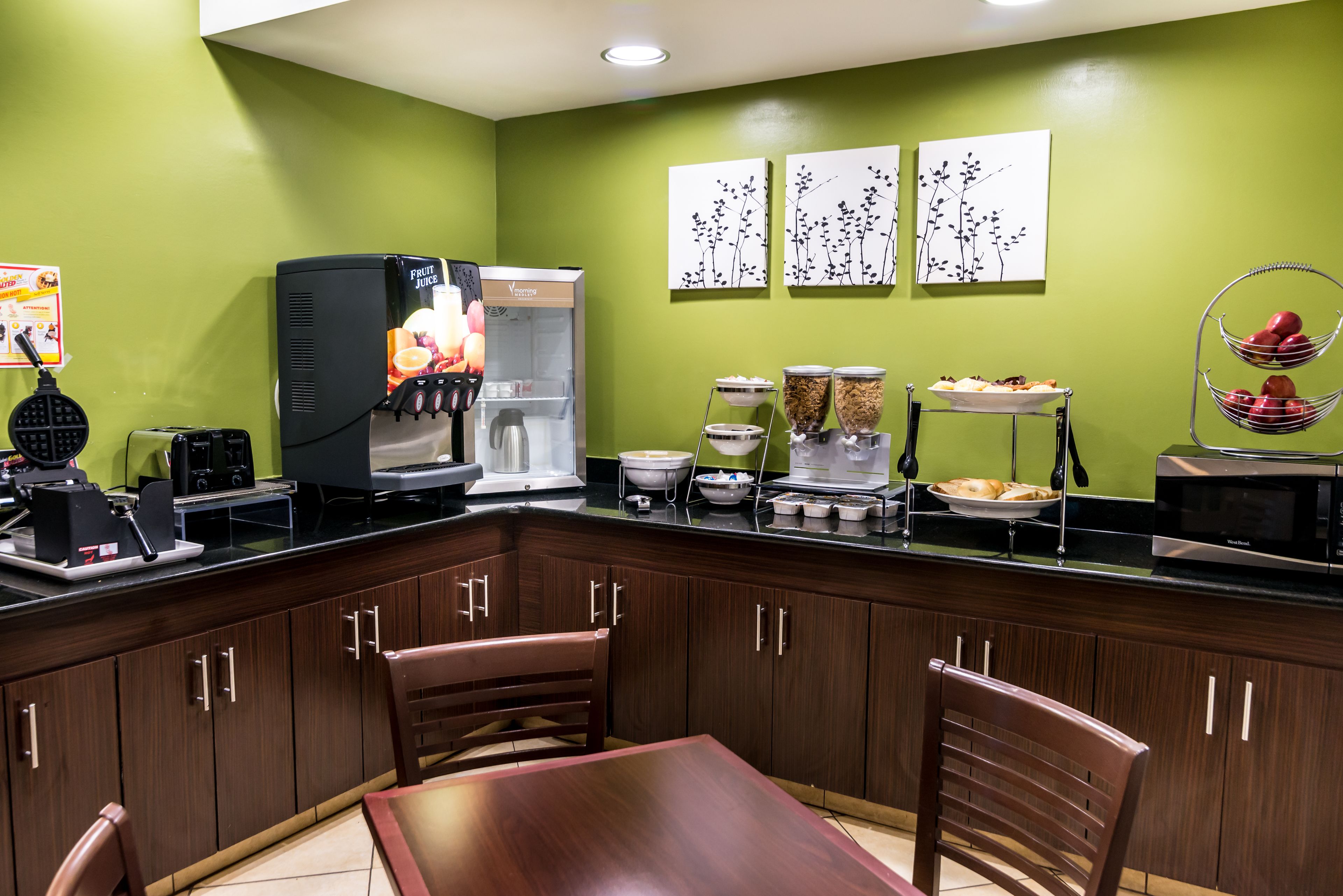 A kitchen with a green wall, a black countertop, and wooden cabinets. There are chairs and a table.