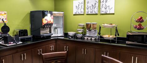 A kitchen with a green wall, a black countertop, and wooden cabinets. There are chairs and a table.