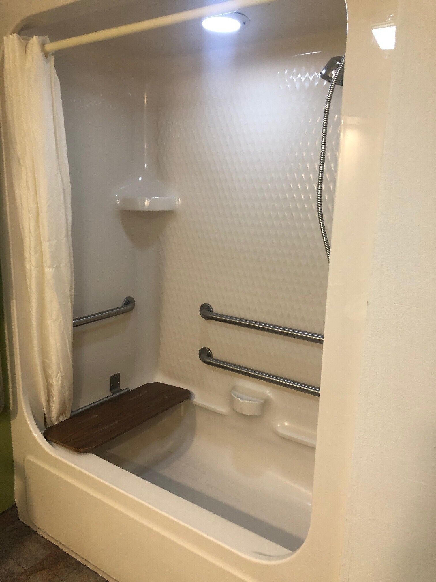 A bathtub with a shower head, grab bars, and a shelf.