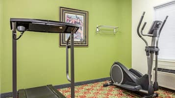 Une salle de sport équipée d’un tapis de course, d’un vélo elliptique et d’un tableau encadré au mur.