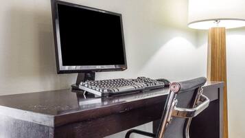 A desk with a computer setup, including a monitor and keyboard, a chair, and a lamp.