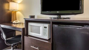 Quarto de hotel com escrivaninha, televisão de tela plana, micro-ondas e luminária.
