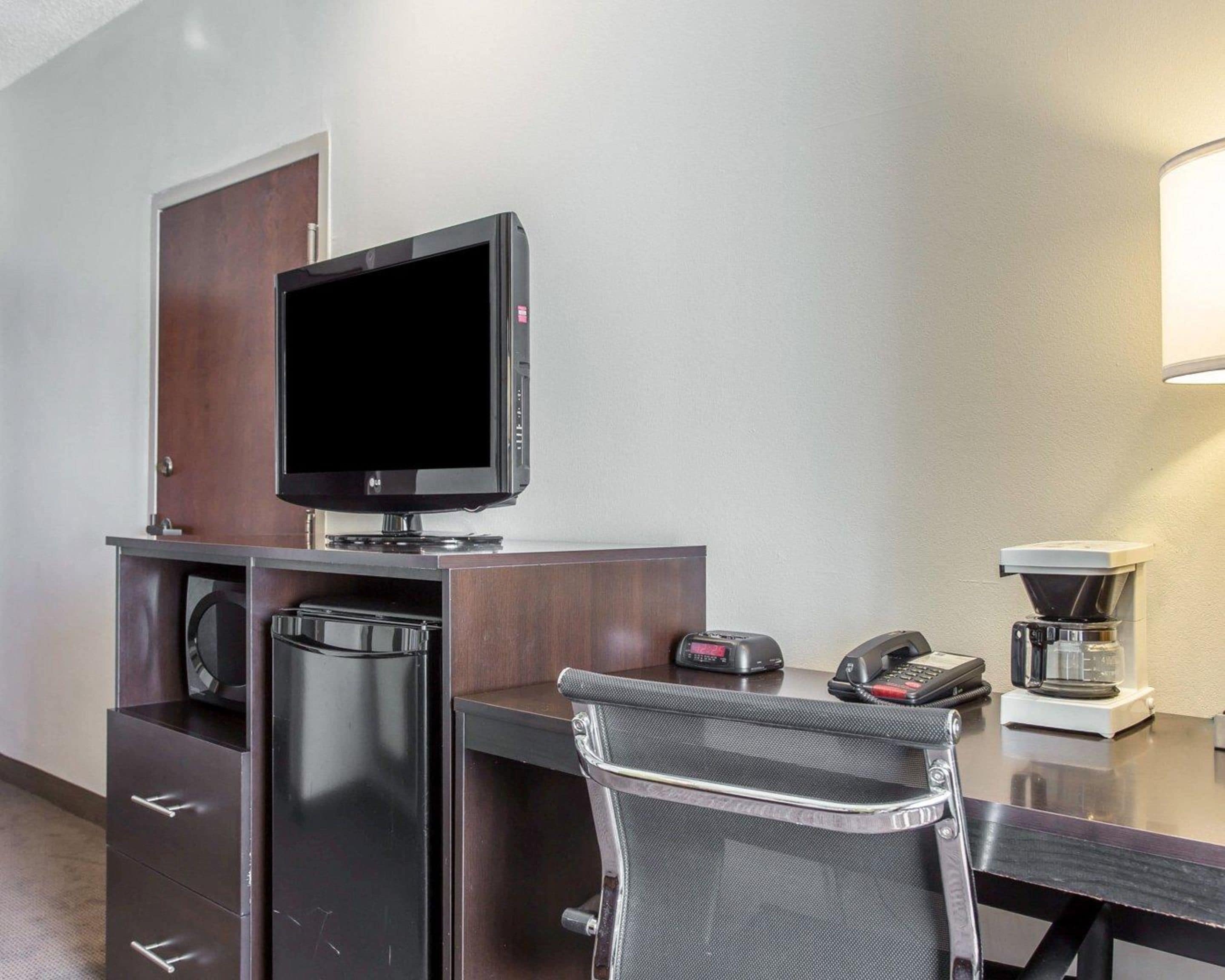 A hotel room with a desk, a flat-screen TV, a coffee maker, and a telephone.