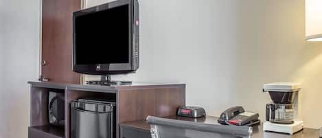 A hotel room with a desk, a flat-screen TV, a coffee maker, and a telephone.