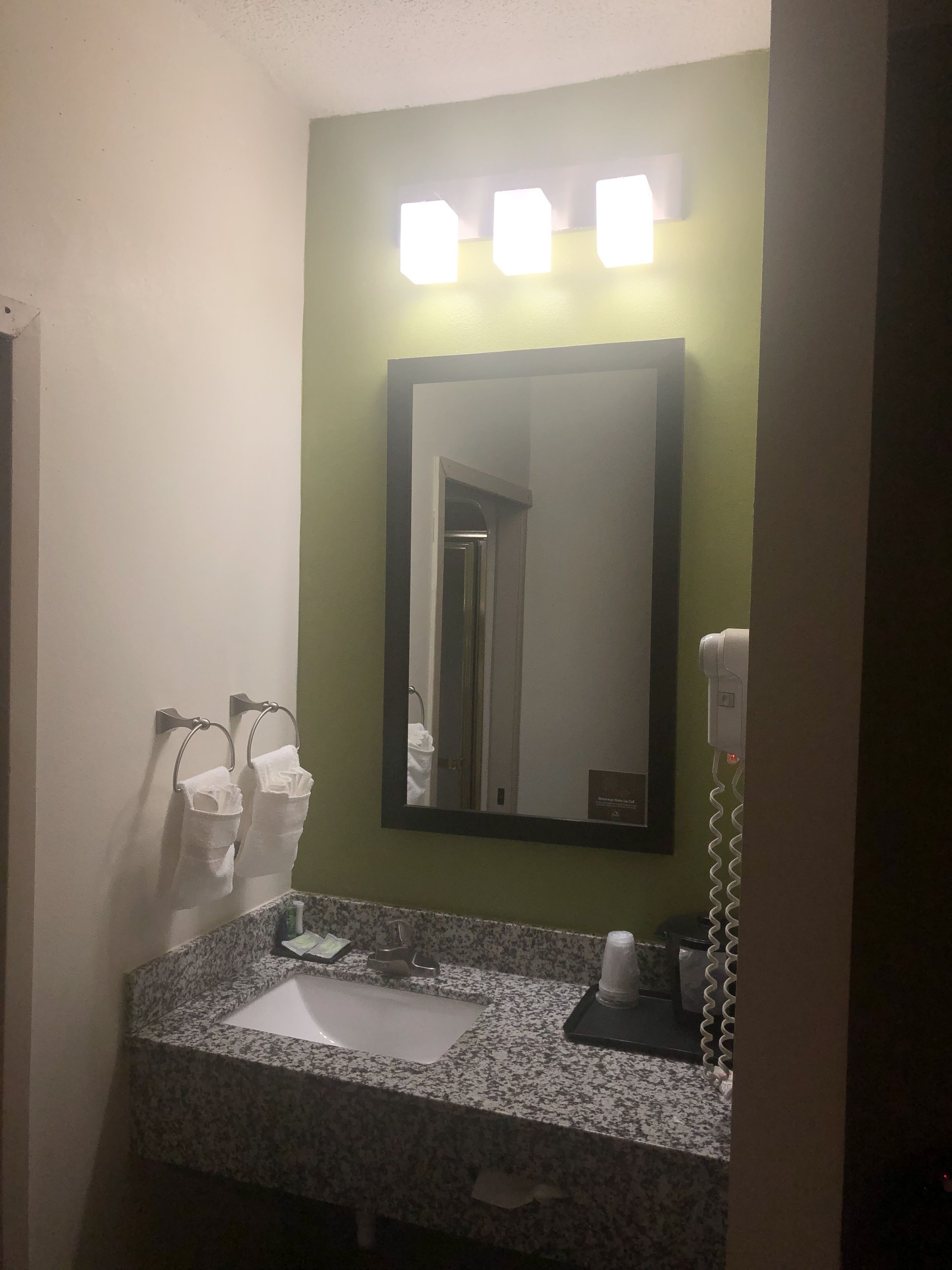 A bathroom with a granite countertop, a sink, a mirror, and a hairdryer on the wall.