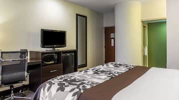 A hotel room with a bed, a desk with a chair, a television, a microwave, and a mirror.