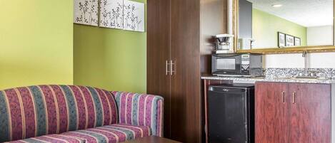 A compact room with a sofa, a small table, a microwave, a refrigerator, and a cabinet.