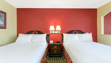Quarto de hotel com duas camas, mesa de cabeceira com luminárias e uma parede com detalhe em vermelho.