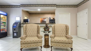 A lobby with two patterned armchairs, a small table with a vase, a Pepsi refrigerator, and an ATM. - Americas Best Value Inn & Suites Sumter (Sumter)