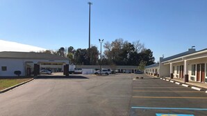 A parking lot with handicap accessible spaces, a building with a 'Welcome' sign, and a row of single-story motel units. - Americas Best Value Inn & Suites Sumter (Sumter)
