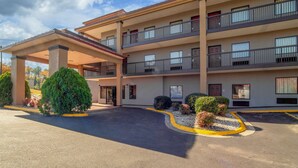 A multi-story hotel with a covered entrance, balconies, and a parking area.