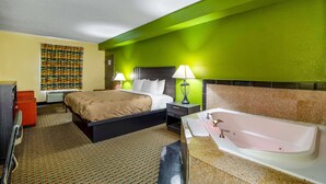 A hotel room with a bed, a nightstand, a desk, a chair, a bathroom with a bathtub, and a patterned curtain.