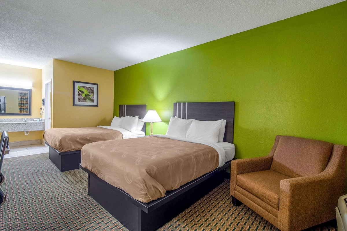 A hotel room with two beds, a green wall, a brown armchair, and a patterned carpet.