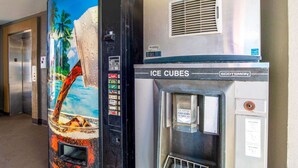 A vending machine with a tropical beach mural, an ice cube dispenser, and a Coca-Cola vending slot.