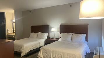 A hotel room with two beds, a desk, a chair, a lamp, and a mirror.