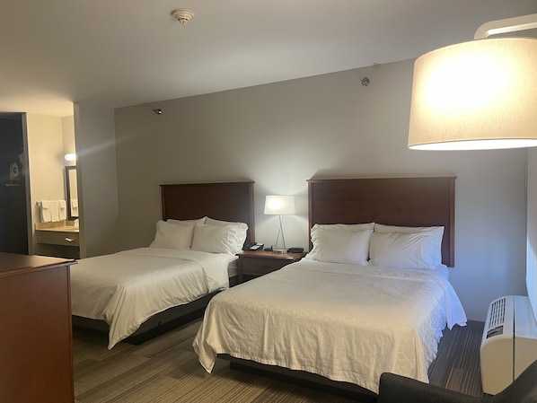 A hotel room with two beds, a desk, a chair, a lamp, and a mirror.