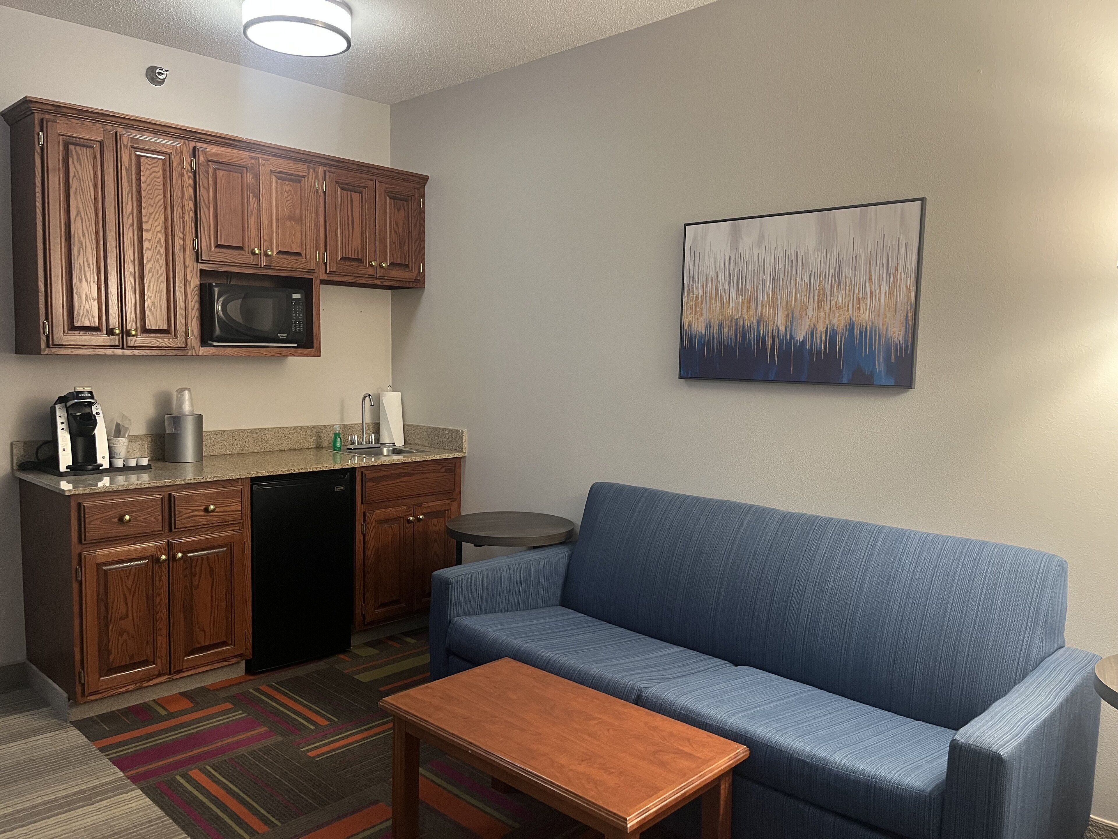 Un espacio habitable compacto con kitchenette, un sofá azul, una mesita y una alfombra colorida.