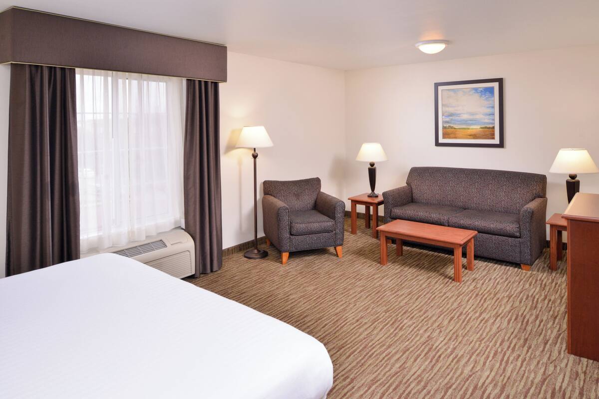 A hotel room with a bed, two armchairs, a sofa, a small table, and a lamp.