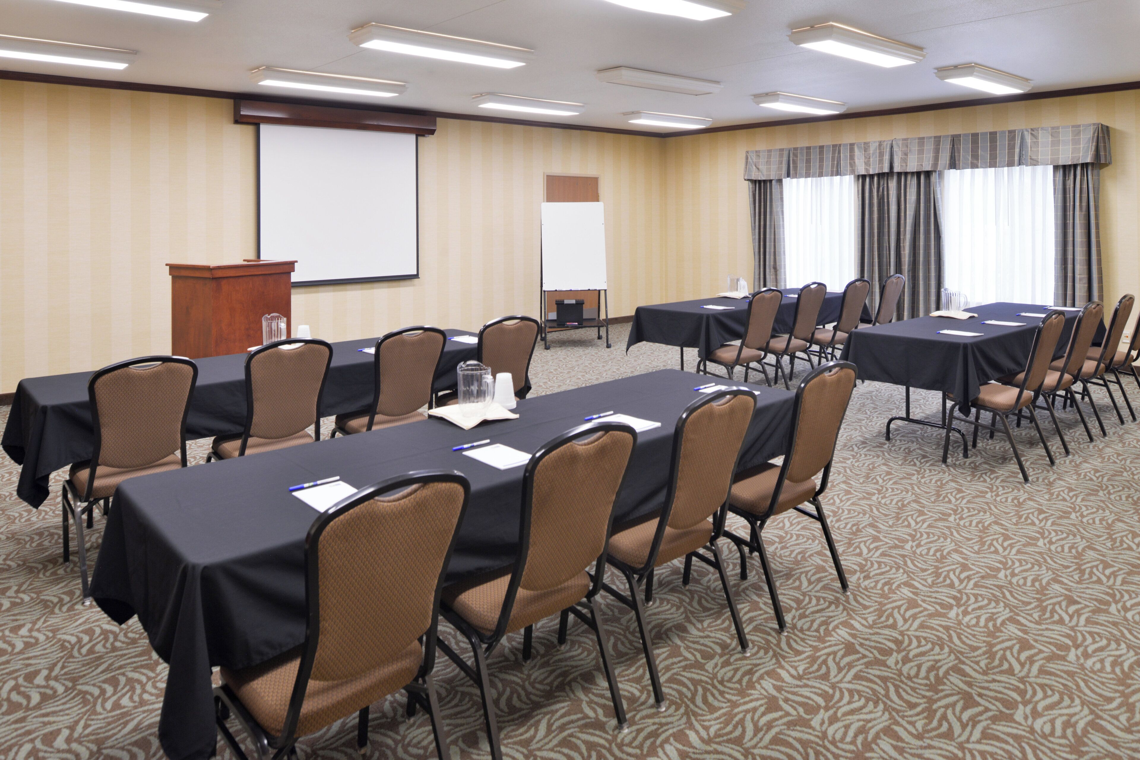 A conference room with multiple tables and chairs, a podium, and a projection screen.