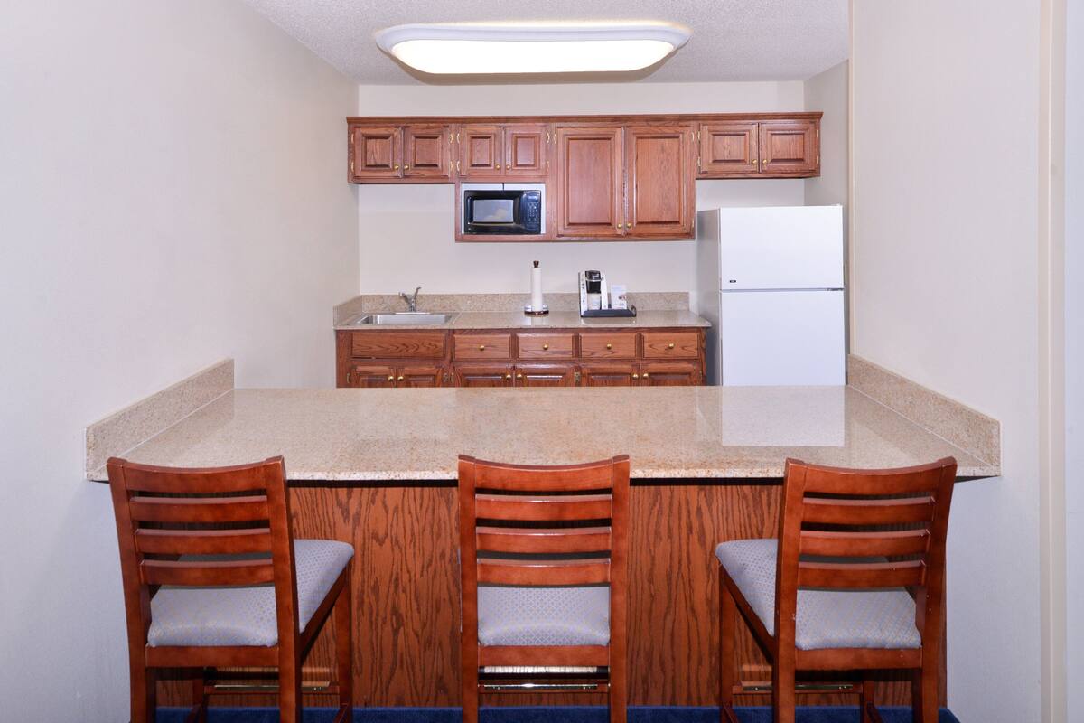 A kitchen with wooden cabinets, a microwave, a refrigerator, a sink, and three bar stools.