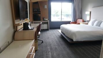 Een hotelkamer met een bed, bureau, stoel, televisie, magnetron en een raam met gordijnen.