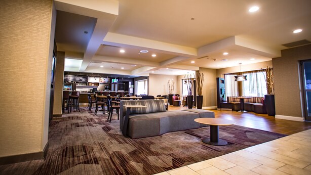 A spacious living area with a sofa, a round coffee table, and a dining area with chairs and a bar. - Courtyard by Marriott Memphis East/Bill Morris Parkway (Memphis)