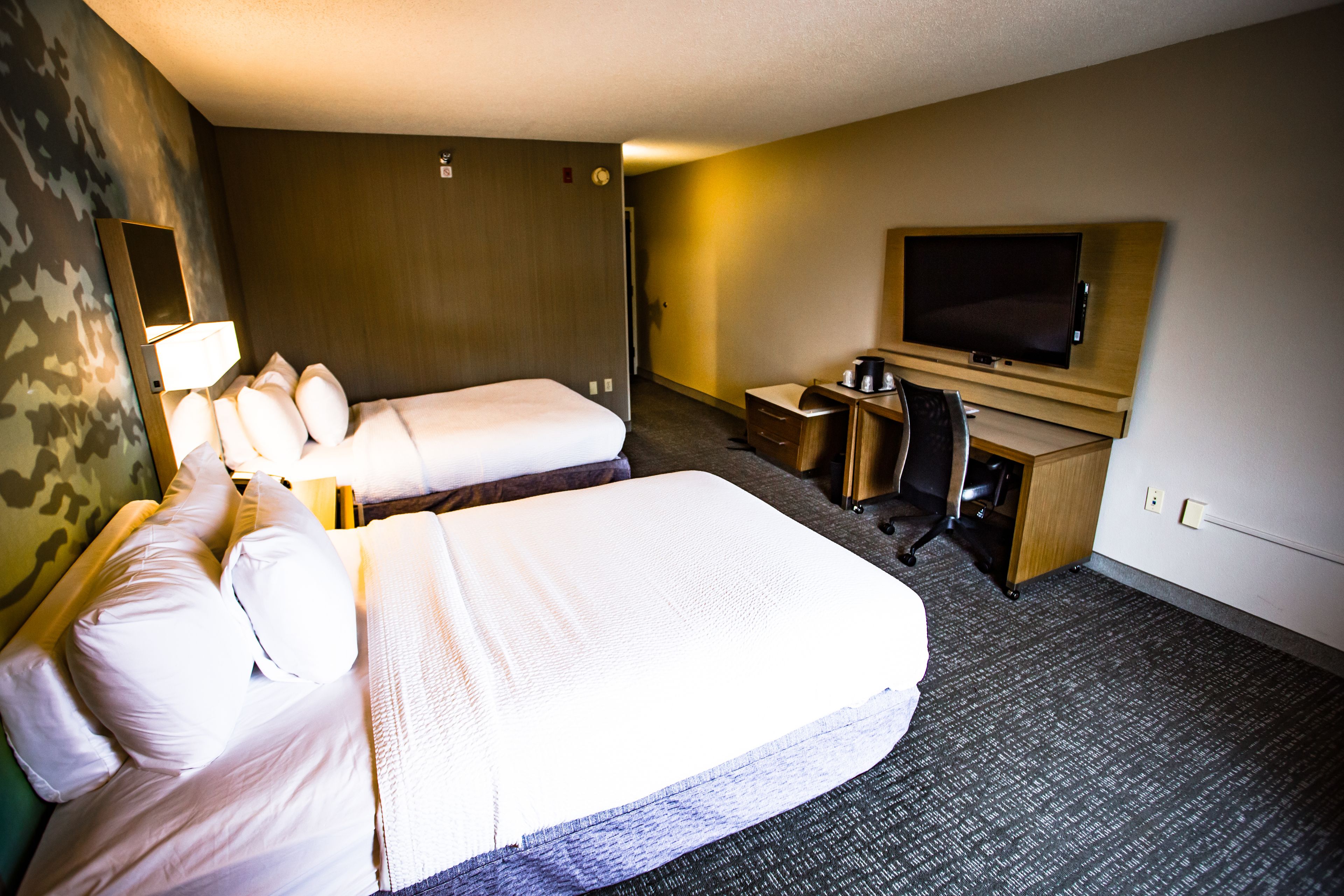 A hotel room with two beds, a desk, a chair, a television, and a mirror.