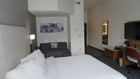A hotel room with a large bed, a desk with a chair, a flat-screen TV, a mirror, and a wall art piece.