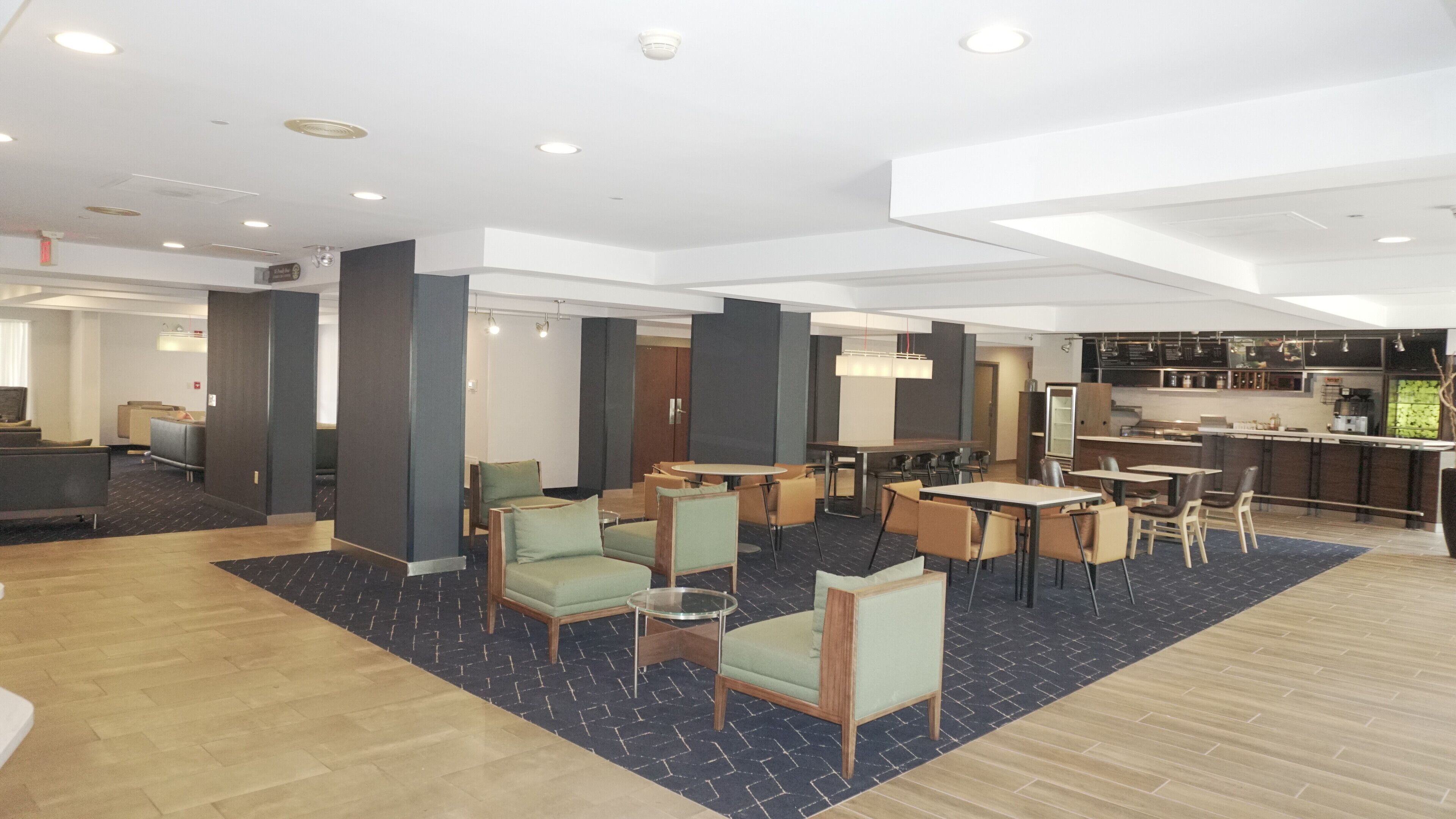 Een ruime hotel lobby met een bar, zitgedeeltes en een zichtbare keuken op de achtergrond.