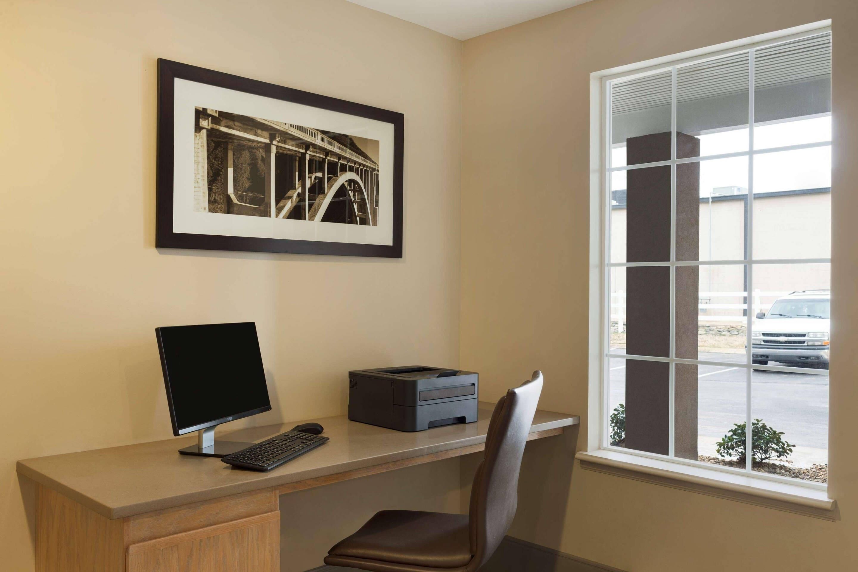 Un espacio de trabajo con escritorio, computadora, impresora y silla. Un cuadro enmarca una imagen en la pared.