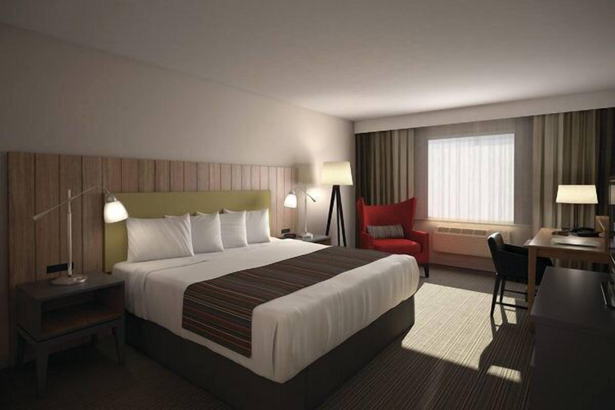 A hotel room with a large bed, bedside tables, a desk, a chair, and a window with curtains.