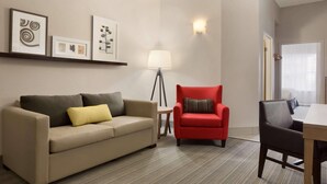 A modern living room with a beige sofa, a red armchair, a small round table with a lamp, and a dining table with chairs. - Country Inn & Suites by Radisson, Jackson, TN (Jackson)