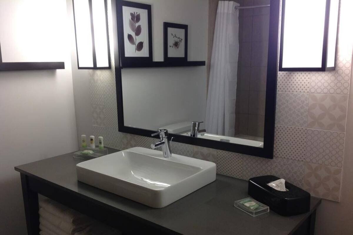 A modern bathroom with a large white sink, a black countertop, a mirror, and a towel rack.