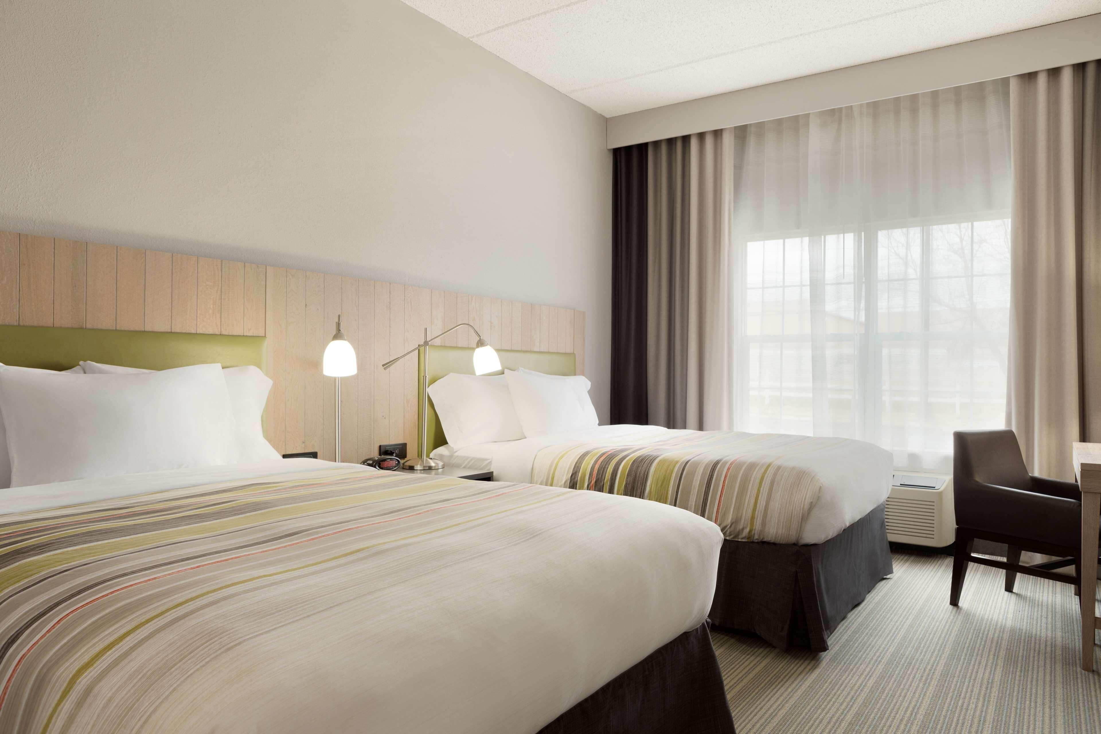 Habitación de hotel con dos camas, un escritorio, una silla y un ventanal con cortinas.