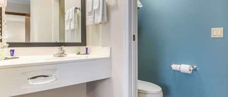 A bathroom with a white vanity, a mirror, a toilet, and a towel rack.
