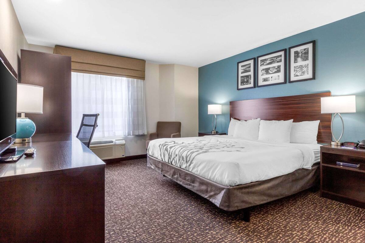 Habitación de hotel con una cama grande, un escritorio con lámpara, una silla y una ventana con cortinas.