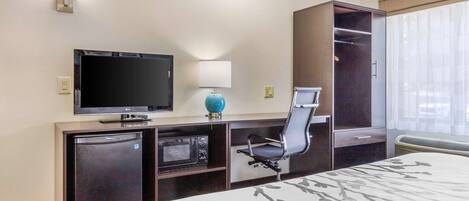 Une chambre d’hôtel équipée d’un lit, d’un bureau avec un ordinateur, d’une télévision, d’un four à micro-ondes et d’une armoire.