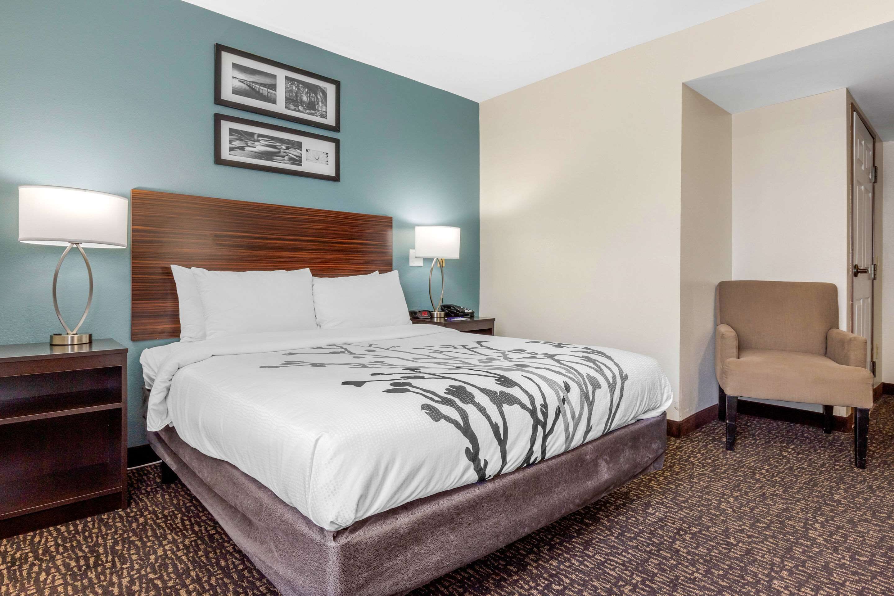 A hotel room with a large bed, two bedside tables with lamps, a chair, and two framed pictures on the wall.