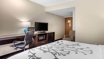 A hotel room with a bed, a desk with a television, a chair, and a microwave.