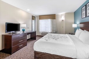 Una habitación de hotel con una cama grande, un televisor en una cómoda de madera, un escritorio y una ventana con cortinas.